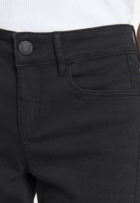 Jean en denim noir avec une texture lisse, doté d'une poche avant et d'un bouton noir circulaire marqué "OPUS". Coupe droite.