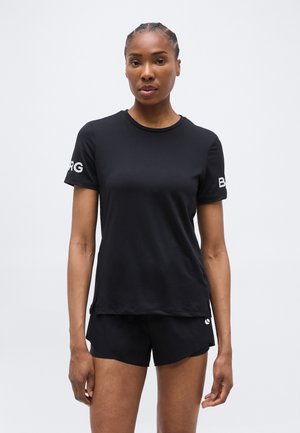 Woman with braided hair wearing black athletic shorts and a black short-sleeve t-shirt with white lettering on the sleeves.