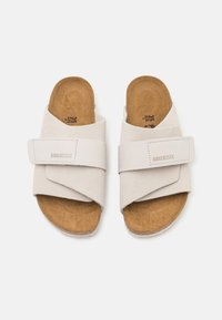 Jasno beżowe sandały Birkenstock z miękką zamszową cholewką, krzyżowym wzorem i teksturowaną korkową wkładką. Regulowany pasek dla lepszego dopasowania.