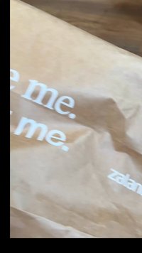 Καφέ χάρτινη σακούλα με τσαλακωμένη υφή, που φέρει λευκό κείμενο "Δες με. Αγάπησέ με. Κράτησέ με." και το λογότυπο "zalando" στη γωνία κάτω.