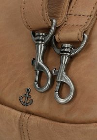 Bruine leren tas met twee zilveren metalen clips, voorzien van een anker-embleem. Een gladde textuur en zichtbare stikdetails zijn aanwezig.