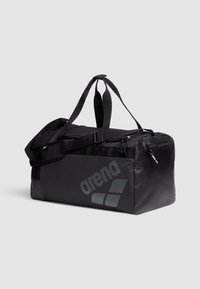 Bolso de deporte negro con un diseño elegante, que presenta un logo prominente, un bolsillo lateral de malla, cremalleras y dos asas de transporte. Material duradero.