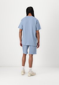 Set di t-shirt e pantaloni corti in cotone azzurro chiaro, caratterizzato da una vestibilità comoda, scollo rotondo e una leggera texture; indossato con sneaker chiare e calzini bianchi.