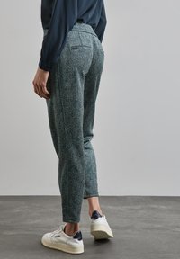 Groene en witte patroontaillebroek met een tapered fit, uitgerust met achterzakken en gecombineerd met witte sneakers. Gladde stoftextuur.