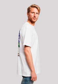 Weißes Baumwoll-T-Shirt mit kurzen Ärmeln, das auf der Rückseite mit einem bunten grafischen Design versehen ist, kombiniert mit blauen Jeans.