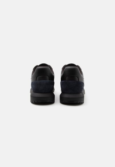 Paire de baskets noires et bleu foncé vues de dos sur un fond gris clair uni.