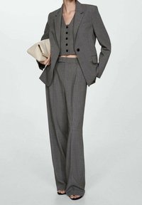 Traje gris de rayas con un blazer ajustado y pantalones de pierna ancha, combinado con un top corto ajustado y complementado con un bolso de mano beige.