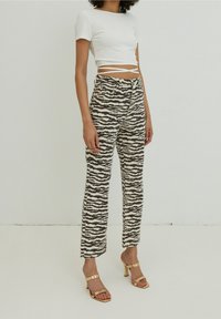 Top corto bianco a costine con spalline laterali, abbinato a pantaloni alti con un motivo a strisce zebra bianco e nero. Sandali con tacco dorato.