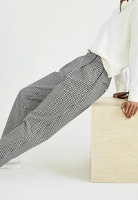 Pantaloni a quadri bianco e nero con una vestibilità ampia, caratterizzati da un alto punto vita e una texture di tessuto morbido, abbinati a una felpa bianca e sneakers.