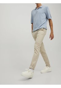 Světle modré polo tričko, béžové slim-fit kalhoty a bílé tenisky. Tkanina vypadá hladce a jemně. Kalhoty jsou mírně ohrnuté na manžetách.