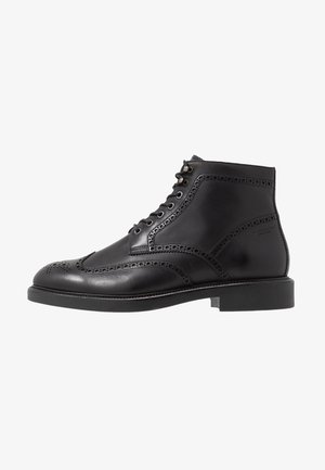 Bottine en cuir noir avec détails brogue, lacets à l'avant et semelle plate en caoutchouc. Texture lisse avec surpiqûres accentuées.