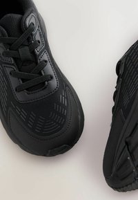 Schwarze Sportschuhe mit strukturiertem Mesh-Obermaterial, flachen Schnürsenkeln, gepolstertem Kragen und Gummisohlen mit musterverzierten Rillen für Traktion.