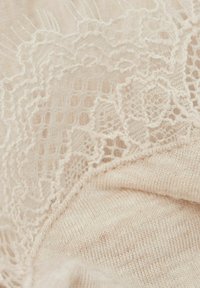 Tekstyl w kolorze kremowym z misternym koronkowym wykończeniem na krawędzi, o miękkiej, gładkiej strukturze dzianiny i subtelnych wariacjach grubości.