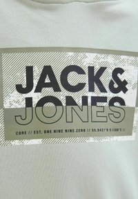 Gaiši zaļa kokvilnas T-kreklu ar lielu grafisku dizainu, kurā melnās burtos ir rakstīts "JACK & JONES" un ir tekstūras svītru akcenti.