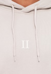 Felpa grigia chiara con cordino, con un logo "II" bianco cucito sul davanti. Tessuto morbido con una finitura testurizzata.