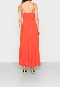 Robes maxi de couleur orange vif, sans manches avec des bretelles spaghetti, corsage smocké, jupe en niveaux et ourlet froncé, assortie à des talons jaunes.