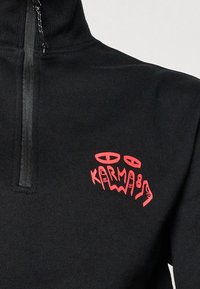 Black sweatshirt with a half-zip design. Features a textured fabric, high collar, and bold red "KARMA" graphic logo on the left chest.