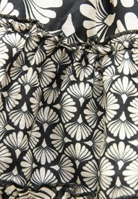 Tissu noir avec motif floral crème, présentant des coutures froncées et des bords volantés.