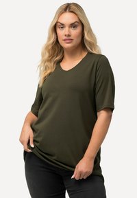 Olijfgroene T-shirt met korte mouwen en V-hals, gemaakt van zachte stof, met een relaxed fit, gecombineerd met donkere jeans.
