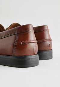 Brune lædersko med et elegant design, der har en tekstureret overflade, kontrasterende syninger og en gummisål med et mønster.