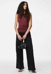 Burgundské bezrúško s nařasenou texturou, doplněné o vysoké černé kalhoty s širokými nohavicemi. Modelka drží malou černou tašku na šňůrku.