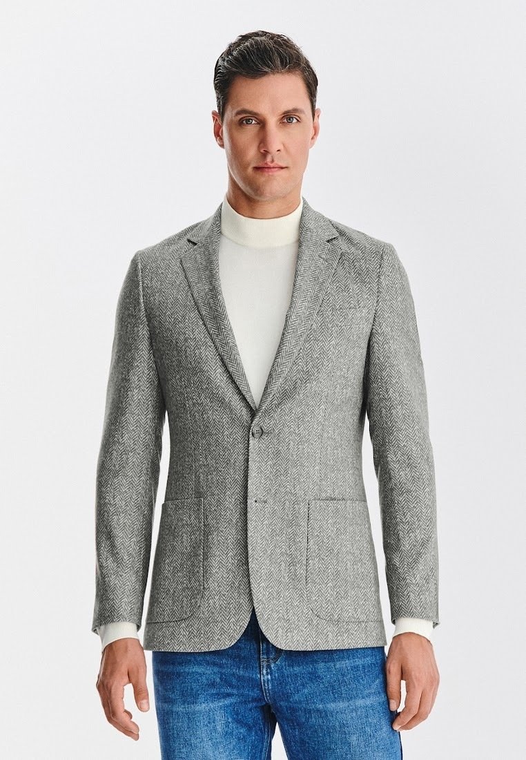 Szary żakiet w jodełkę z klapami, dwoma przednimi kieszeniami i zapięciem na guziki, w połączeniu z jasnym golfem. Dżinsy.