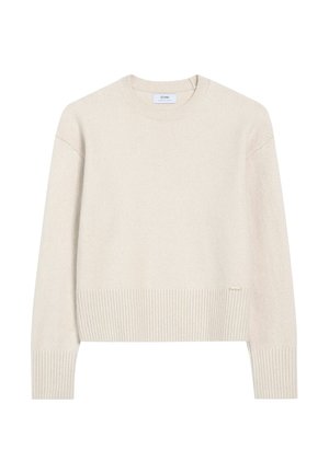 Kremowy sweter wykonany z miękkiego materiału dzianinowego, z okrągłym dekoltem, ściągaczami na rękawach i u dołu, z małą metką marki z boku.