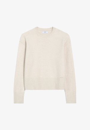 Kremowy sweter wykonany z miękkiego materiału dzianinowego, z okrągłym dekoltem, ściągaczami na rękawach i u dołu, z małą metką marki z boku.