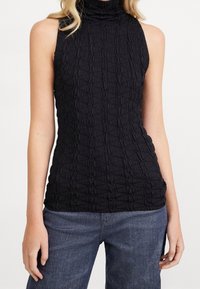Czarny top bez rękawów z teksturowanej, pomarszczonej tkaniny z wysokim kołnierzem i dopasowanym krojem, zestawiony z ciemnoniebieskimi dżinsami.