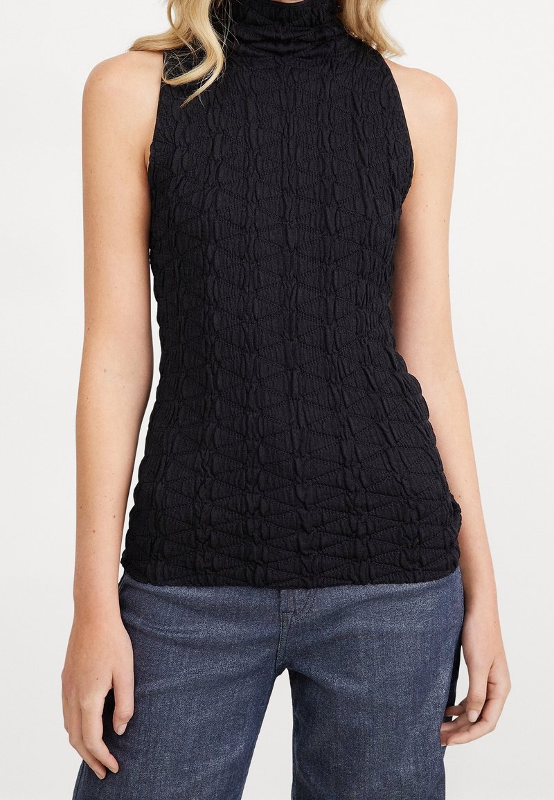 Czarny top bez rękawów z teksturowanej, pomarszczonej tkaniny z wysokim kołnierzem i dopasowanym krojem, zestawiony z ciemnoniebieskimi dżinsami.