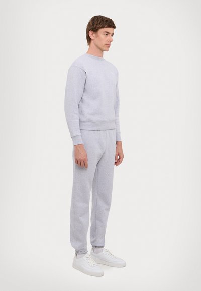 Lichtgrijze sweatshirt met ronde hals en elastische manchetten, gedragen met bijpassende joggers met elastische tailleband en manchetten, gecombineerd met witte sneakers.