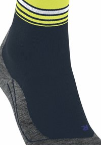 Zbliżenie na ciemnonavy skarpetę z szarym piętą i palcem, z żółtymi i białymi paskami u góry, zaprojektowaną do odzieży sportowej.