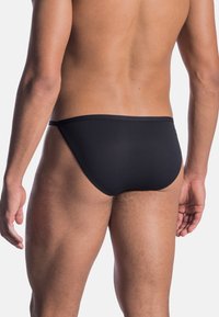 Schwarze Schwimmshorts mit einer glatten Textur, minimaler Bedeckung und einem elastischen Bund, die ein körperbetontes Design und klare Linien präsentieren.