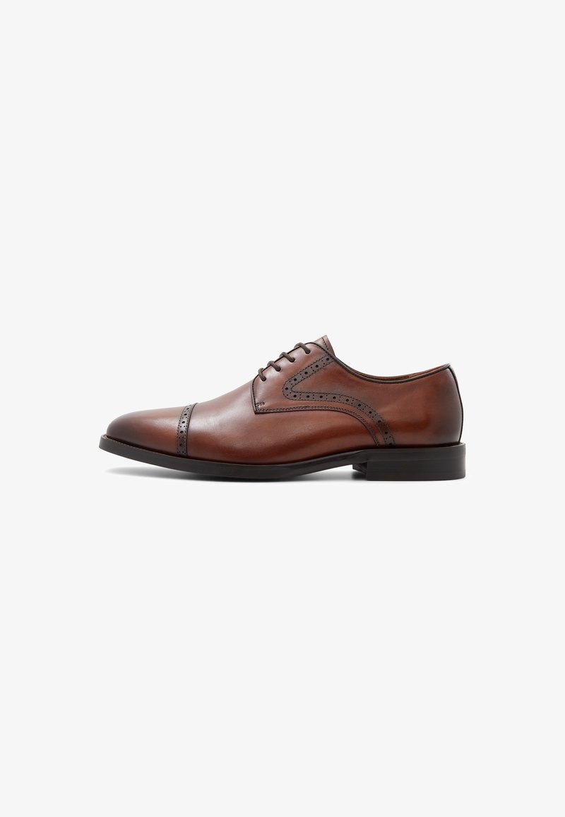 Chaussure habillée Oxford pour homme en cuir marron avec des détails brogués et une semelle noire, vue de côté sur un fond blanc.