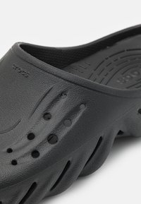 Crne Crocs sandale s teksturiranim finišem, s ventilacijskim otvorima i zakrivljenim dizajnom. Izrađene su od laganog materijala s širokim, otvorenim prstima.