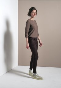 Bruine trui, zwarte skinny jeans en lichtgroene sneakers. De trui heeft lange mouwen en een ronde hals. Eenvoudig ontwerp, geen patronen.
