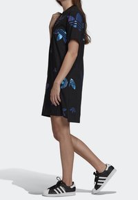 Svart oversized t-shirt klänning med flerfärgade fjärilsmotiv och korta ärmar. Kombineras med svartvita sneakers med tre ränder.