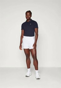 Tumesinine polo särk lühikeste varrukatega, valged lühikesed püksid ja valged spordijalatsid. Üksikasjalik disain nööbiga kraega ja diskreetne logo rinnal.