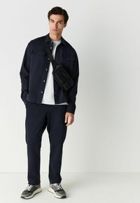 Camisa azul marino de botones con dos bolsillos en el pecho, combinada con pantalones a juego. Bolso cruzado negro, zapatillas deportivas grises y blancas. Camiseta blanca lisa.
