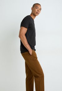 Black short-sleeve t-shirt paired with brown trousers, featuring a smooth texture and straight fit. Subtle seams and comfortable pockets visible.