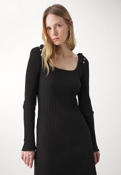 Rochie neagră cu mânecă lungă, cu decolteu pătrat. Dispune de umeri strânși, cu accente decorative și o silueta ajustată.
