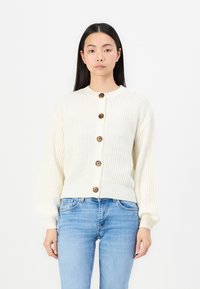 Cardigan tricoté en crème avec une texture côtelée, doté d'un col rond, de manches longues et de cinq boutons marron sur le devant.