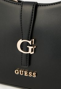 Borsa a mano in ecopelle nera con logo "G" lucido color oro e scritta "GUESS" in rilievo. Caratterizzata da una forma strutturata e dettagli cuciti.