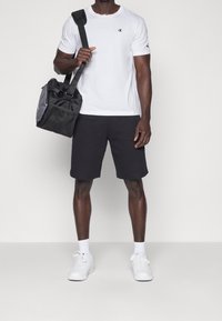 Vit bomull t-shirt med logotyp, svarta shorts, vita sneakers och en svart tote bag. Enkelt design och bekväm passform.