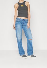 Gray crop tank top with flame graphic, paired with light blue straight-leg jeans featuring a knee tear and worn denim texture. Gray sneakers.