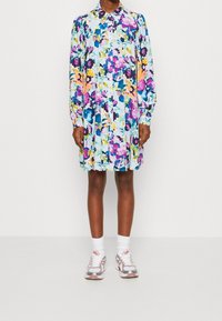 Blommig skjortklänning i pastellfärger, med knäppning fram, långa ärmar och avslappnad passform. Matchas med vita strumpor och sportiga sneakers.