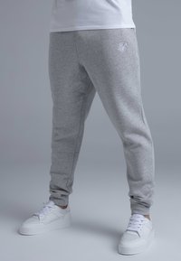 Grey sweatpants made of soft fabric with a tapered fit, featuring embroidered logo detail and elastic cuffs. Worn with white sneakers.