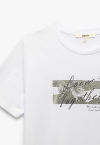 Camiseta de algodón blanca con mangas cortas, que presenta un diseño gráfico en texto plateado y negro que dice "Amor Juntos" con un fondo texturizado.