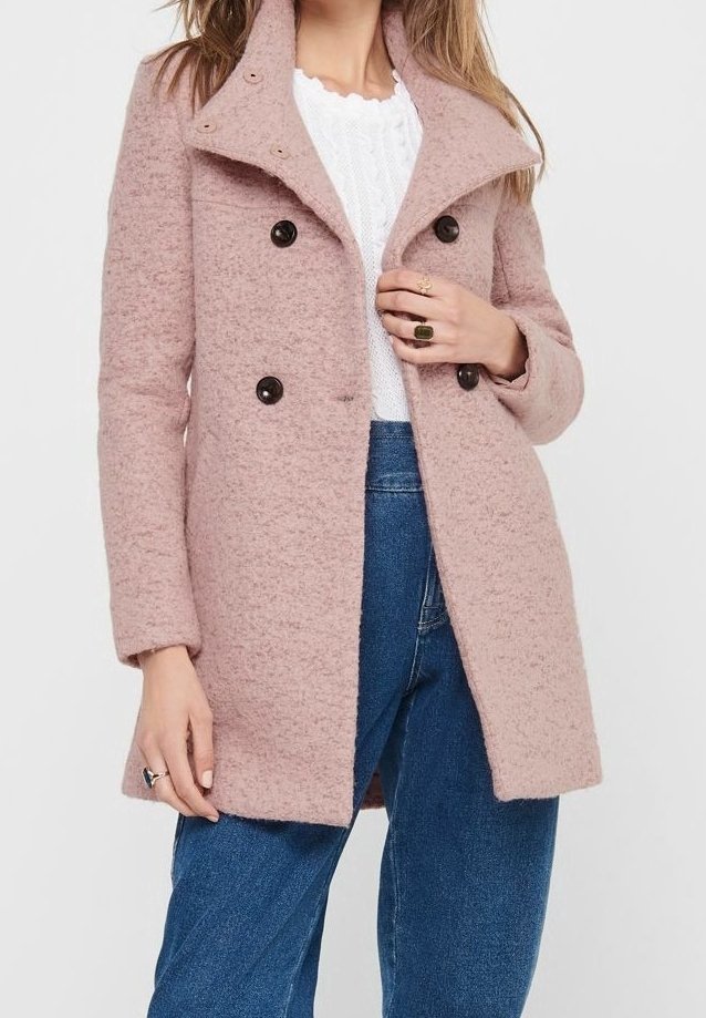 Cappotto doppio petto in misto lana rosa con grandi bottoni neri, colletto a punte e finitura testurizzata, abbinato a un maglione bianco e jeans.