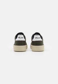 Tenis texturizados verdes com solas de borracha creme e abas de calcanhar brancas marcadas "VEJA". Apresenta um design de cano baixo e um colarinho acolchoado.